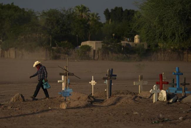 A Yaqui Indigenous wears a bandana over his mouth as he walks through dust past the cemetery where slain water-defense leader Tomás Rojo is buried in Potam, Mexico, on Tuesday, Sept. 27, 2022. (AP Photo/Fernando Llano)