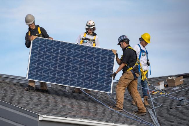 Workers wearing Iron & Earth clothing set up solar panels. Photo courtesy of Iron & Earth / Facebook