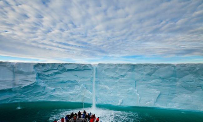 Under a blanket of clouds, tourists watch a meltwater waterfall on an icecap. Photograph: Ralph Lee Hopkins/National Geographic Society/Corbis