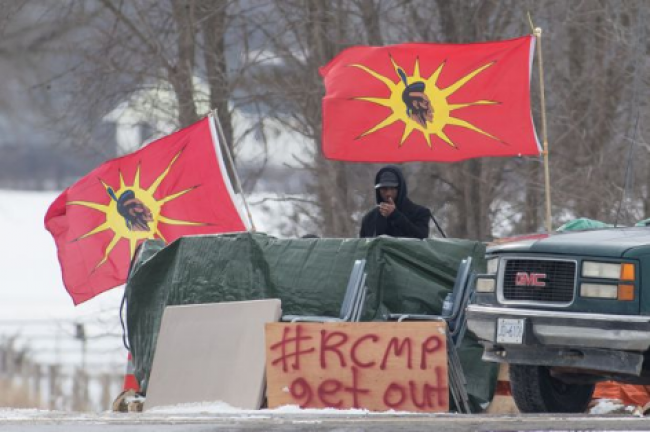 A protester stands between Mohawk Warrior Society flags at a rail blockade on the 10th day of demonstration in Tyendinaga, near Belleville, Ont., Sunday, Feb. 16, 2020. LARS HAGBERG/THE CANADIAN PRESS
