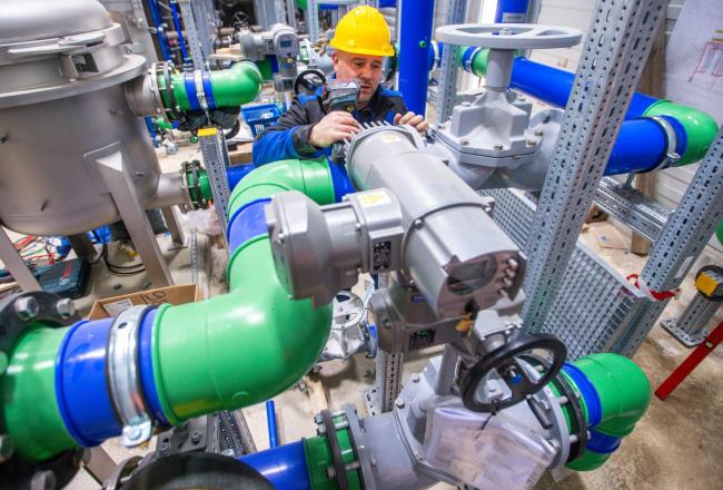A fitter installs blue plastic pipes in the thermal solenoid room of a deep geothermal power plant. (PHOTO BY JENS BÜTTNER/PICTURE ALLIANCE VIA GETTY IMAGES)