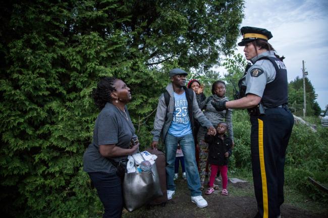 A group of seven people from Nigeria are informed in July 2017 by an RCMP officer of their rights and the law they're breaking by crossing illegally from the U.S.A. into Canada at Roxham Road, Que. (Photograph by Roger LeMoyne)
