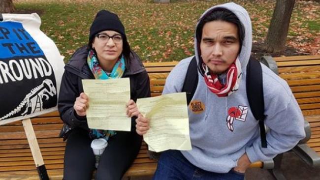 Sadie-Phoenix Lavoie and Kevin Settee hold up their court papers after they were ticketed for trespassing at Parliament Hill in Ottawa on Monday. (Sadie-Phoenix Lavoie/Facebook)