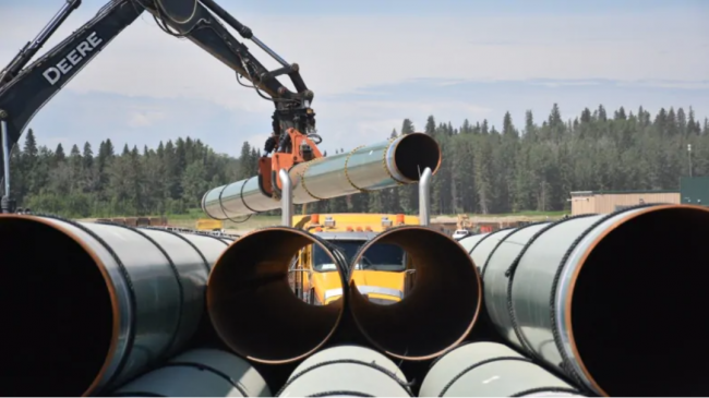 A picker unloads pipe from a truck and stacks it in a Trans Mountain yard in Edson, Alta. (Terry Reith/CBC)