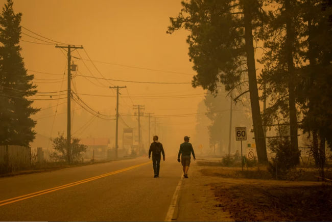 Two men walk along a road in Scotch Creek, B.C., as wildfire smoke fills the air on Aug. 19, 2023. (Ben Nelms/CBC)