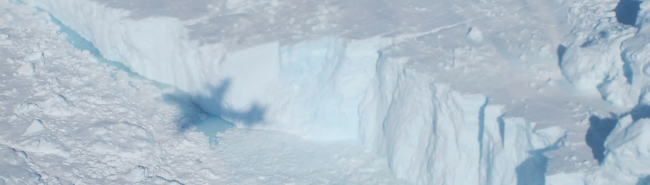 A NASA P-3 airborne laboratory plane casts a shadow on the calving front of Jakobshavn Glacier in Greenland, during a 2014 “Operation Ice Bridge” survey flight to study the Earth’s polar ice. Public domain image courtesy NASA / Jim Yungel via Wikimedia Commons. www.nasa.gov/icebridge