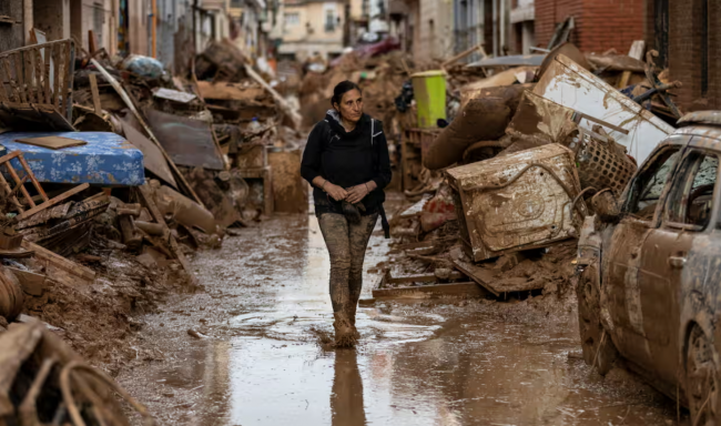 A woman walks through a flooded street in Valencia, Spain. The effects of the climate crisis are likely to have a much bigger impact on economic wellbeing than previously thought, a report by actuaries said. Photograph: Pablo Blázquez Domínguez/Getty Images