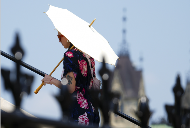A person uses an umbrella for shade as they walk on Parliament Hill in Ottawa in June, 2024. Advocates say that the potential impacts of climate change on Canadian retirement plans has been understated by the country's chief actuary. Photo by: Sean Kilpatrick / The Canadian Press