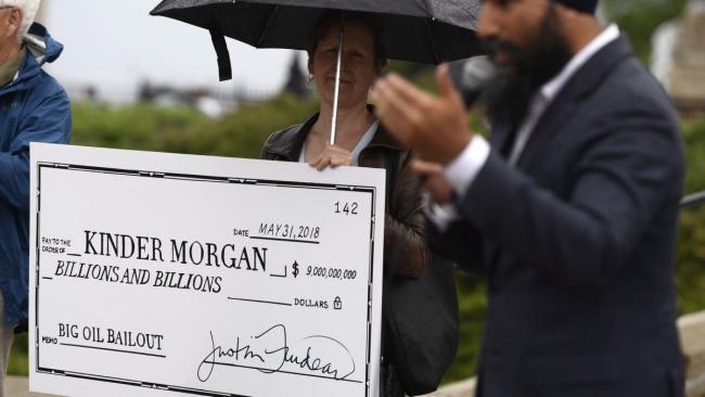 NDP Leader Jagmeet Singh speaks as a woman holds a novelty cheque made out to Kinder Morgan at a rally against the proposed Trans Mountain pipeline project, on Parliament Hill in Ottawa on Tuesday, May 22, 2018. THE CANADIAN PRESS/Justin Tang
