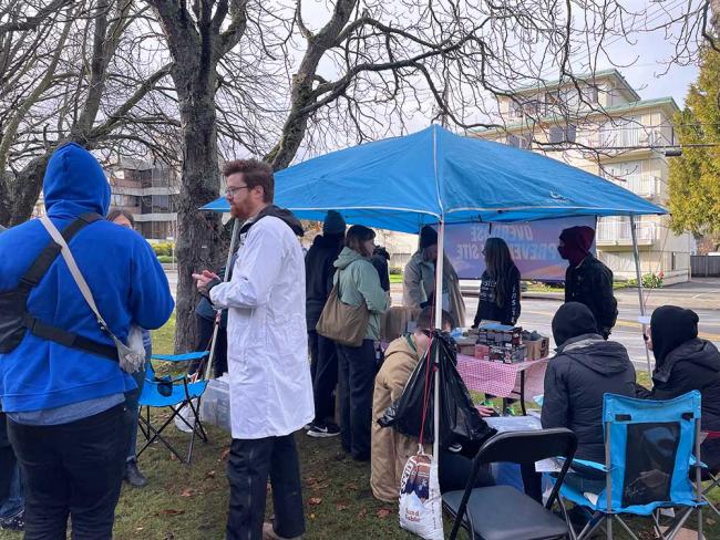 After Dr. Ryan Herriot, in the white coat, opened a pop-up overdose prevention site on Royal Jubilee Hospital grounds today, the site was moved off hospital grounds by hospital security teams to city property. Photo by Brishti Basu.