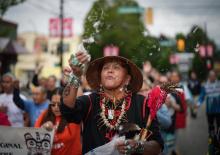 Randy Tait, of the Nisga'a-Gitxsan Nation, blows down feathers into the air during a friendship walk to a National Indigenous Peoples Day gathering, in Vancouver, BC, Wednesday, June 21, 2023. Photo by: Darryl Dyck / The Canadian Press