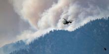 A helicopter prepares to make a water drop as smoke billows along the Fraser River Valley near Lytton, British Columbia, Canada, on July 2, 2021. Photo: James MacDonald/Bloomberg via Getty Images