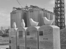 A memorial to schoolchildren killed in the Great East Japan Earthquake of 2011 stands next to silos used to store wood pellets at a new thermal electricity plant in Sendai. Photo submitted.